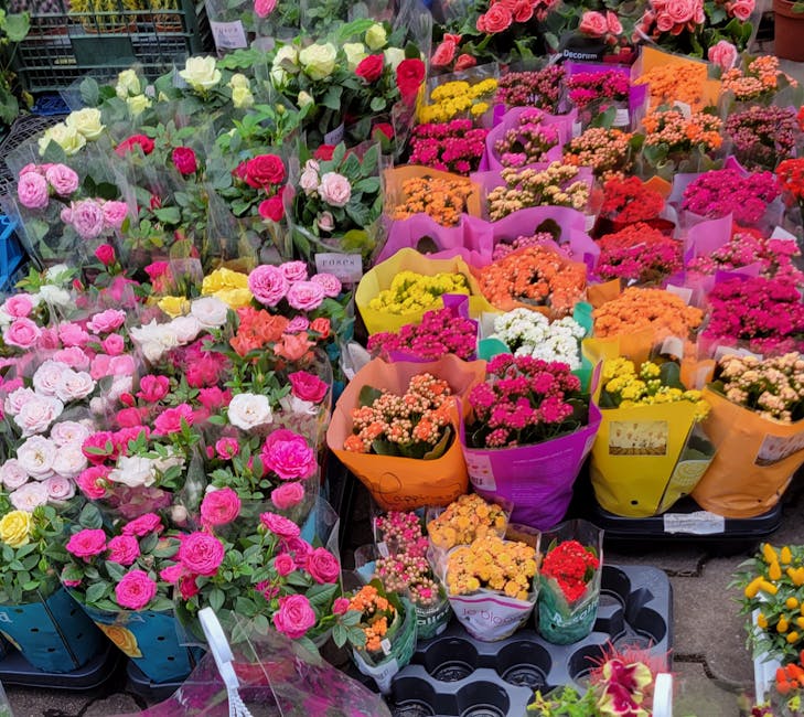 A vibrant display of fresh flowers arranged in bouquets at a florist shop. The arrangement includes pink, white, yellow, orange, and red roses, along with clusters of small pink, yellow, and orange bl