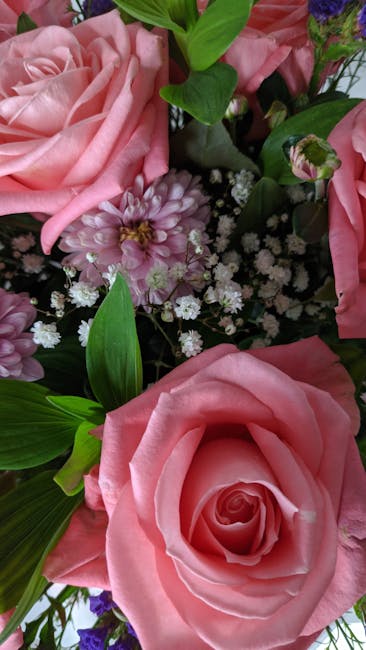 A close-up view of a floral arrangement featuring large, soft pink roses with gently curled petals, complemented by small, delicate white baby’s breath flowers and vibrant green leaves with a smooth