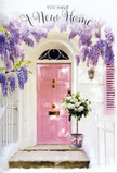 This softly lit doorway scene in Ilford portrays a home being quietly but beautifully introduced to its new chapter through flowers and colour. The central focus is a tender pink front door, painted in a calm, matte finish that absorbs the light and radiates a gentle warmth, standing out against the surrounding whitewashed walls. Next to it, a pastel-toned shutter mirrors the shade, creating a sense of balance that feels both modern and nostalgic, reminiscent of the quietly charming side streets off Green Lane. Above, generous sprays of wisteria spill down in layers, their blooms a blend of lavender, lilac, and soft violet hues. The dangling flower clusters and trailing green vines create a natural arch over the entrance, suggesting a fragrant, almost storybook-like frame that anyone stepping up to the doorway must pass through. At ground level, a grey, vintage-style metal bucket is positioned neatly in front of the door. This unassuming vessel holds an opulent bouquet of white and cream roses, the blossoms round and full, arranged closely so that petals brush and overlap, evoking plushness and depth. Delicate green foliage threads itself through the arrangement, adding subtle twists of texture and colour around the ivory blooms. A silky pink ribbon is tied around the bucket, the bow slightly off-centre, its flowing ends resting gently on the step and echoing the door's blush tones. The resulting scene feels like a heartfelt greeting, perhaps prepared for someone moving into their first Ilford home near Valentines Park or Clements Road. It conveys the emotional mix of excitement, tenderness, and reassurance that a local florist such as Flower Delivery Ilford understands so well when helping mark a new beginning with flowers.